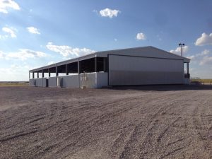 A large, open-sided metal barn or warehouse, ideal for office and industrial manufacturing, stands on a gravel lot under a sunny sky. With wide entrances, this structure is perfect for any construction project managed by a skilled general contractor. -Lopp Construction